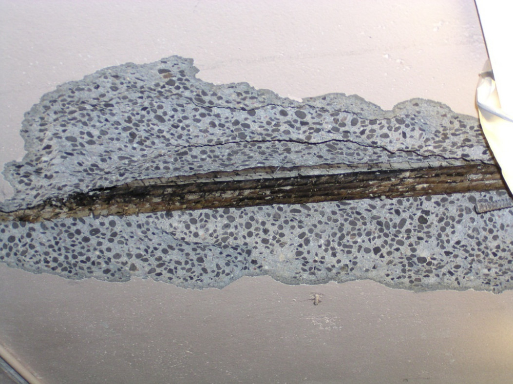 Severe corrosion of a paper-wrapped tendon causing concrete spalling on the underside of an old post-tension slab.